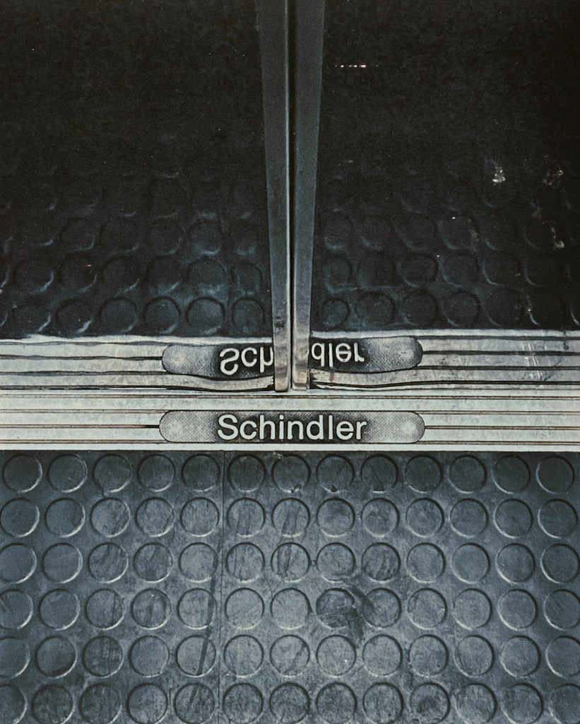 Close-up of an elevator threshold with "Schindler" engraved on the floor plate. Scuffed rubber floor.