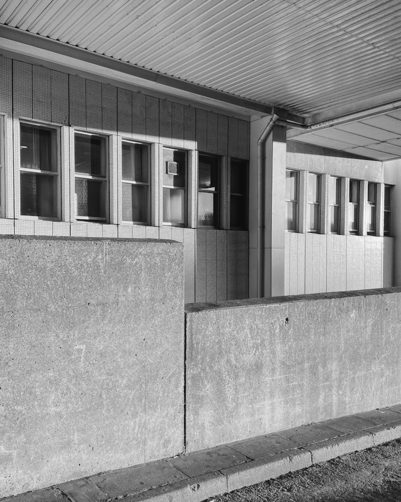 Black and white image of brutalist building with rectangular windows, concrete walls and a covered walkway.
